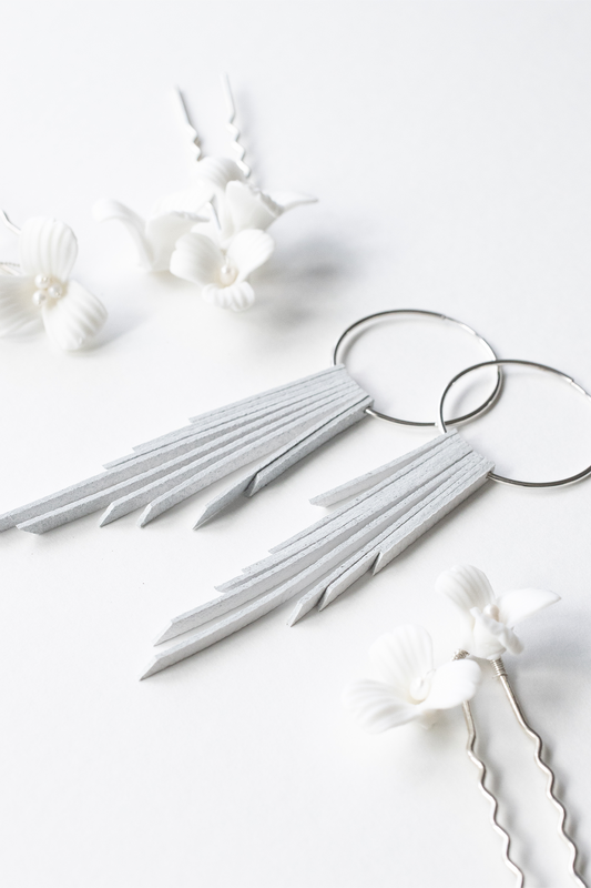 White leather fringe wedding earrings with sterling silver hoops resting on a white backdrop with white floral hair pins