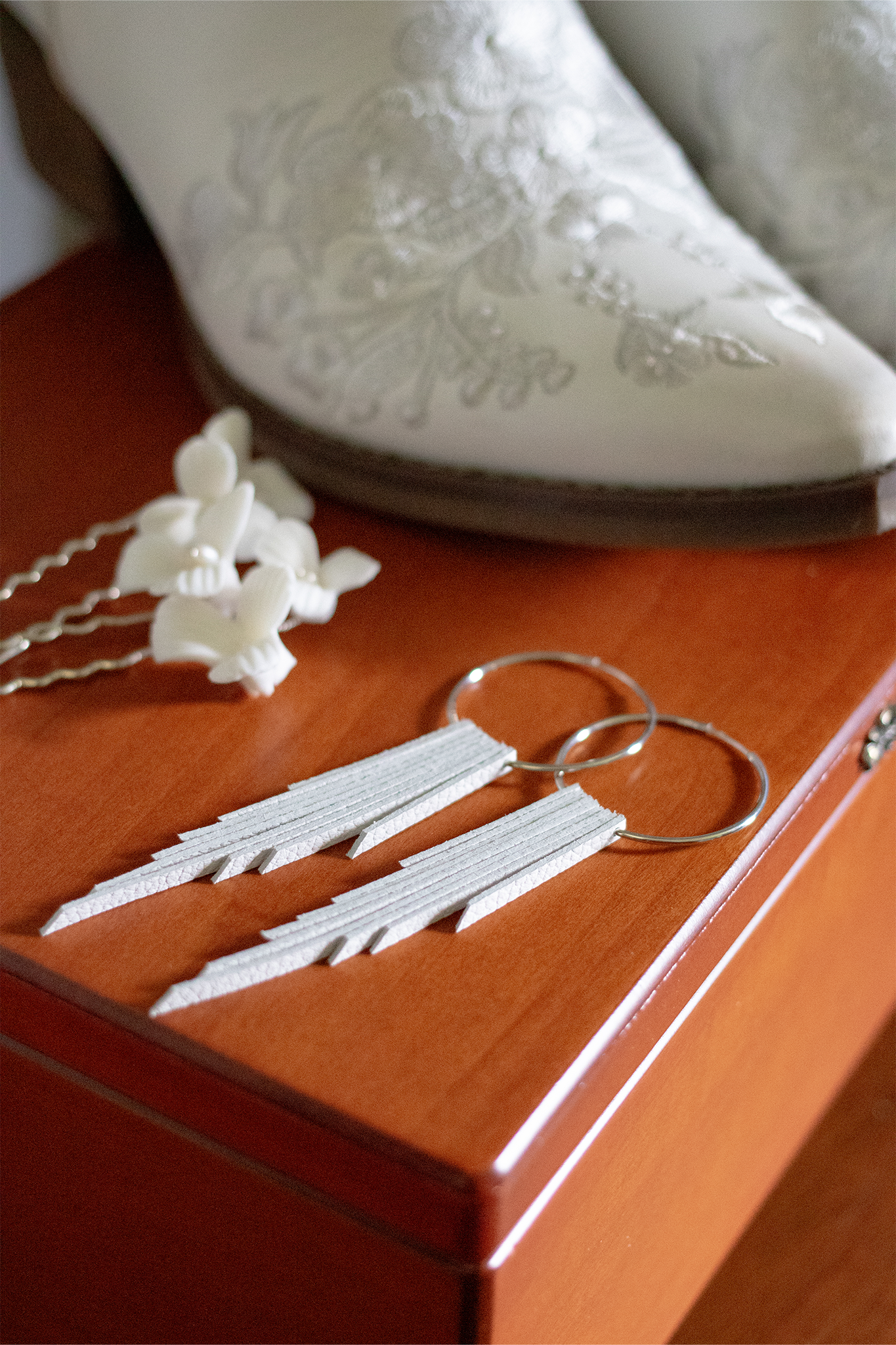 White leather fringe earrings with silver hoops, styled with floral hair pins and embroidered white cowboy boots.