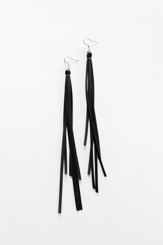 Black leather fringe dangle earrings resting on a white backdrop