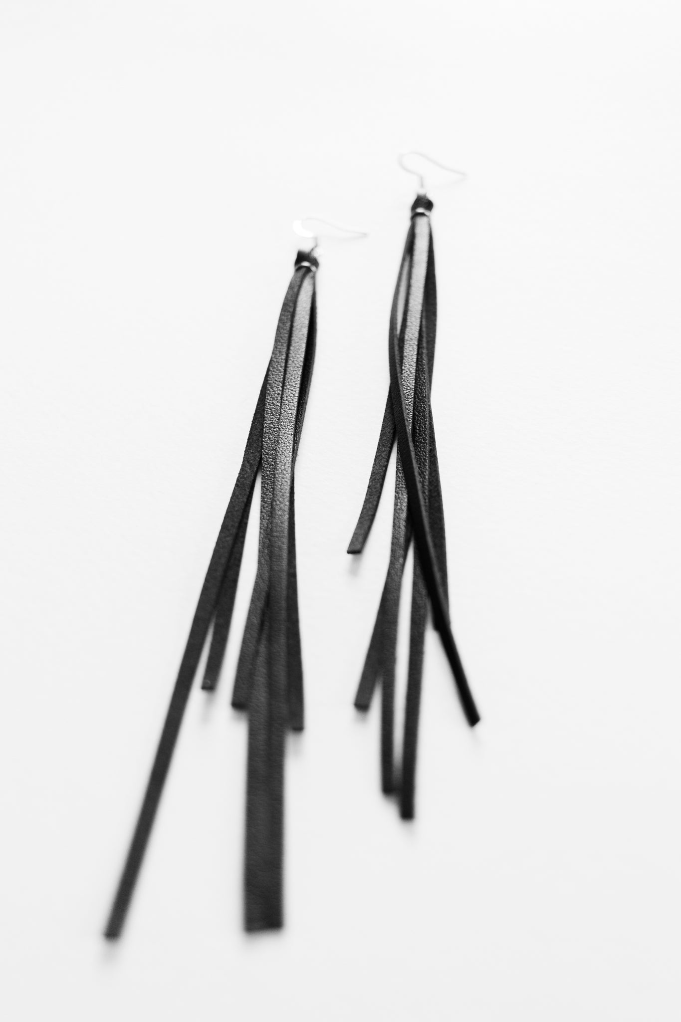 Black leather fringe dangle earrings resting on a white backdrop