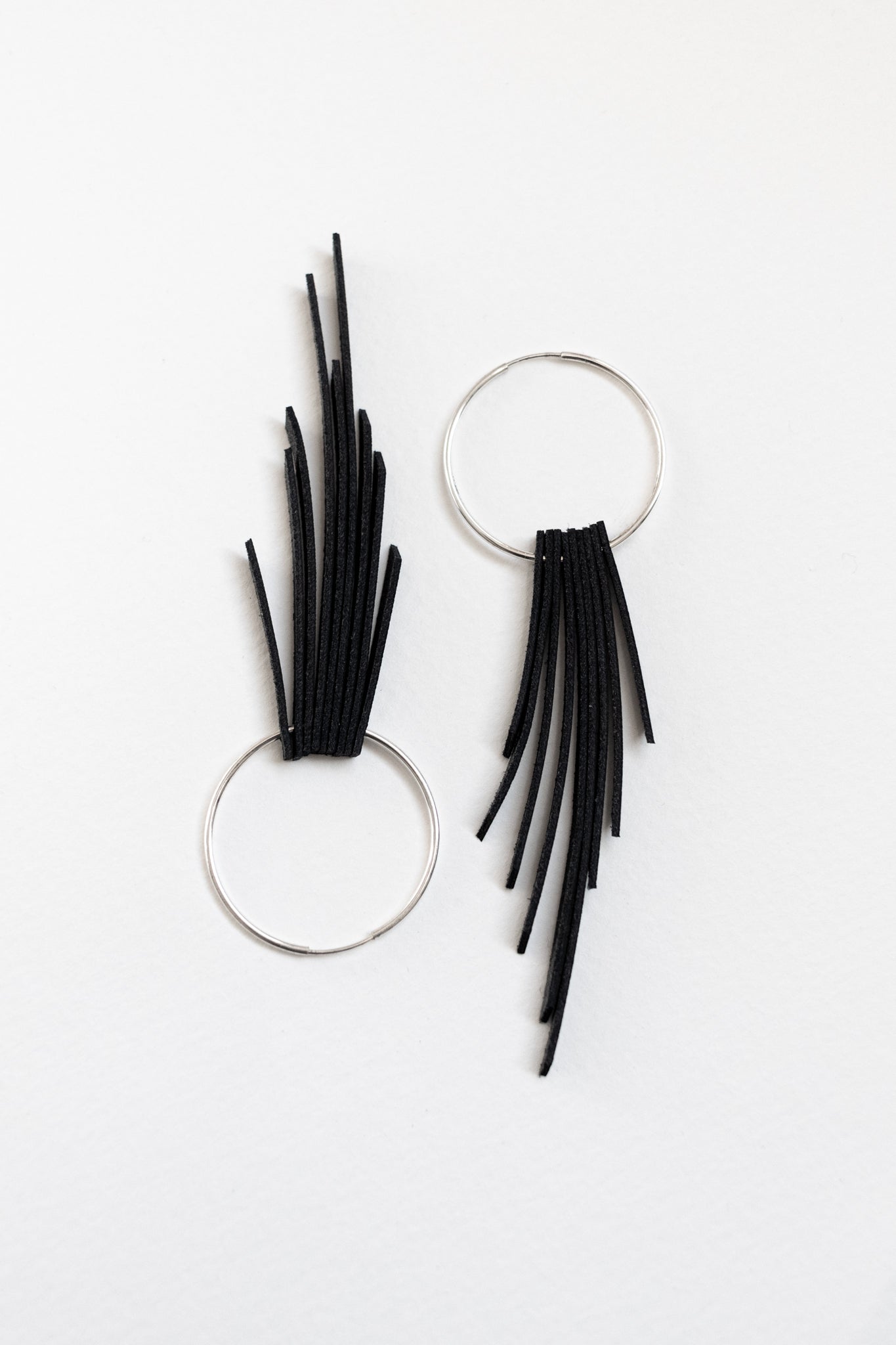 Black leather fringe earrings with sterling silver hoops resting on a white backdrop