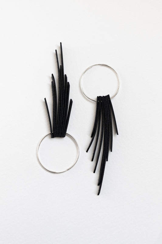 Black leather fringe earrings with sterling silver hoops resting on a white backdrop